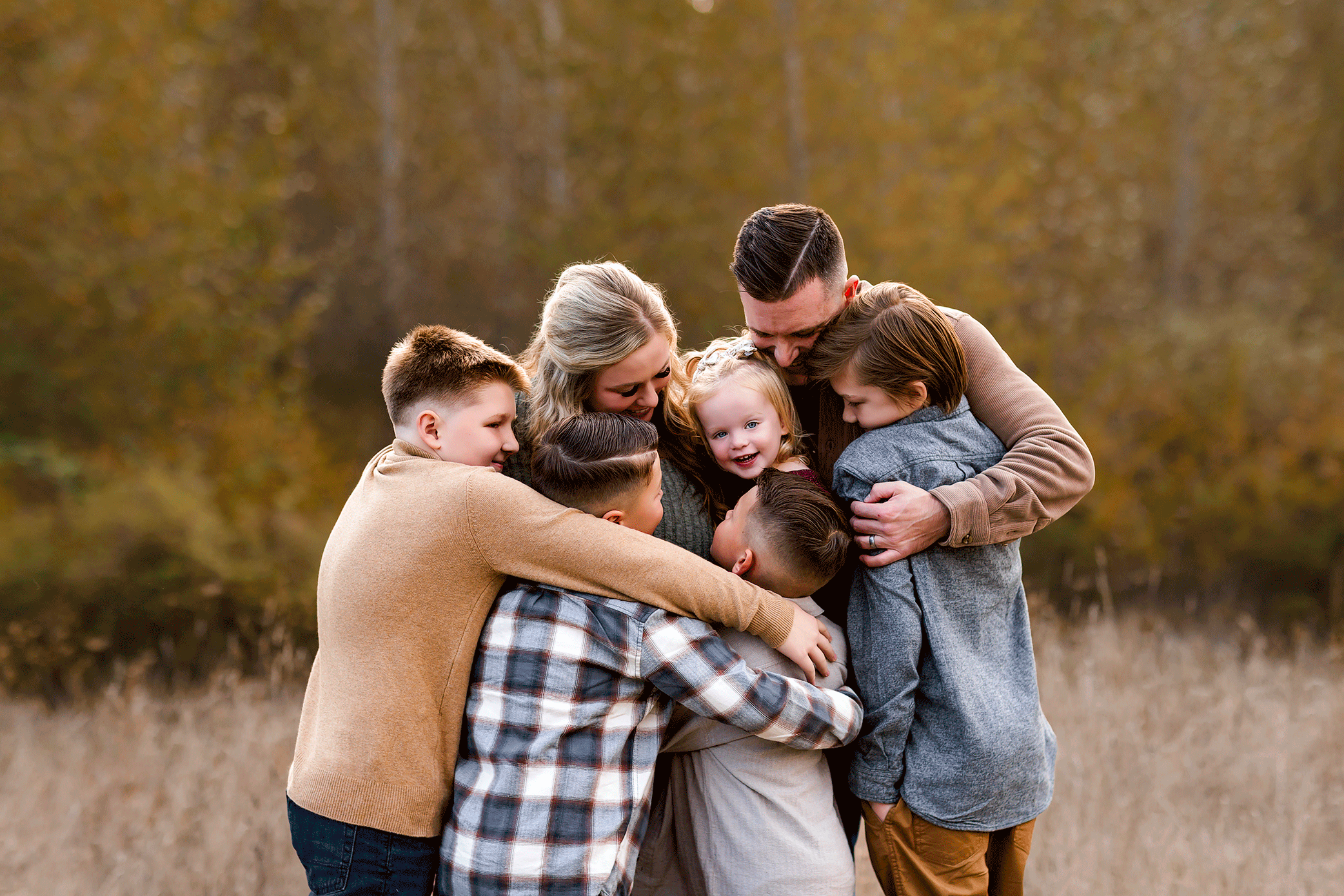 Large family gathered in a joyful group hug in a field at sunset.