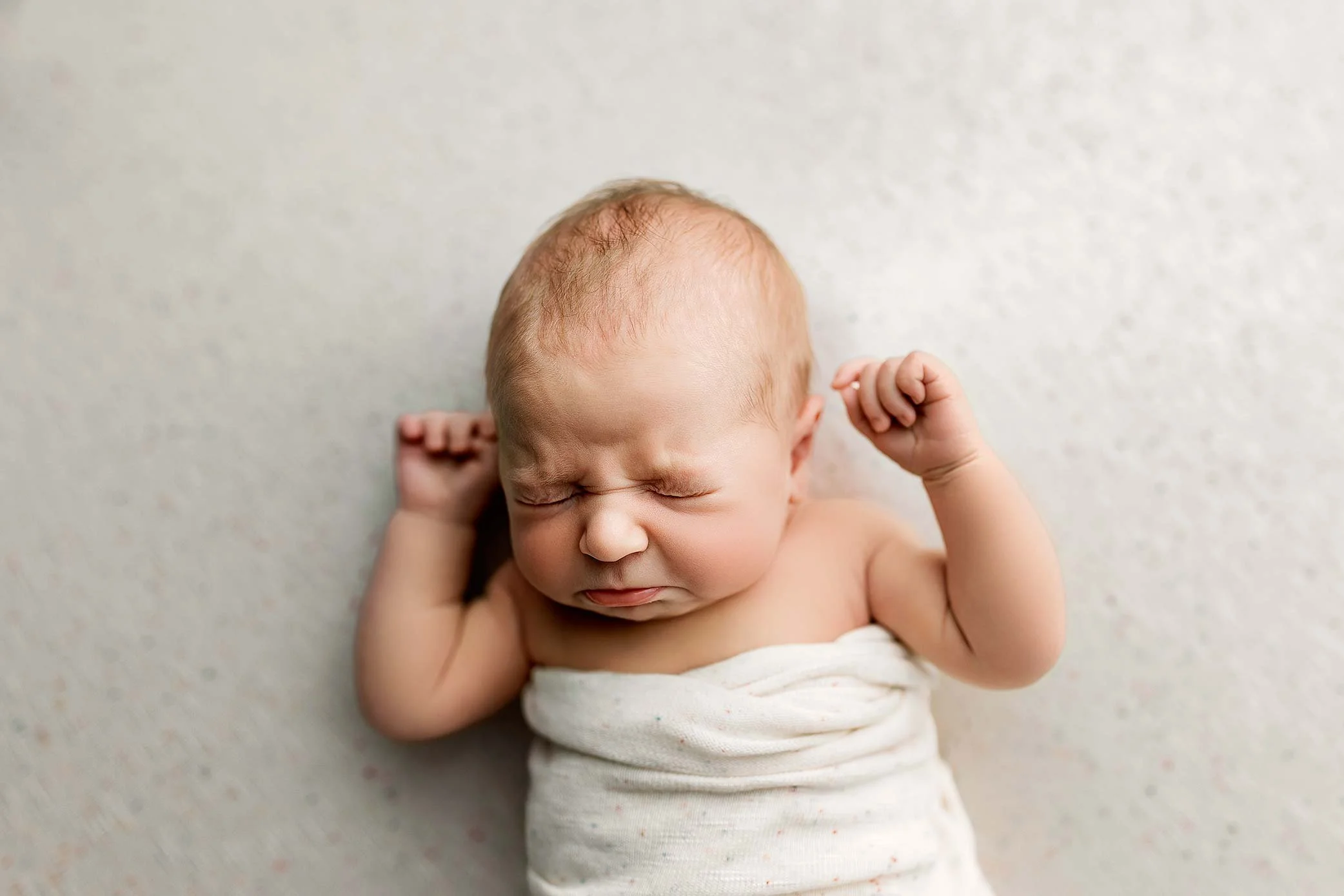 Newborn baby mid sneeze during a natural moment captured in a newborn photography session.