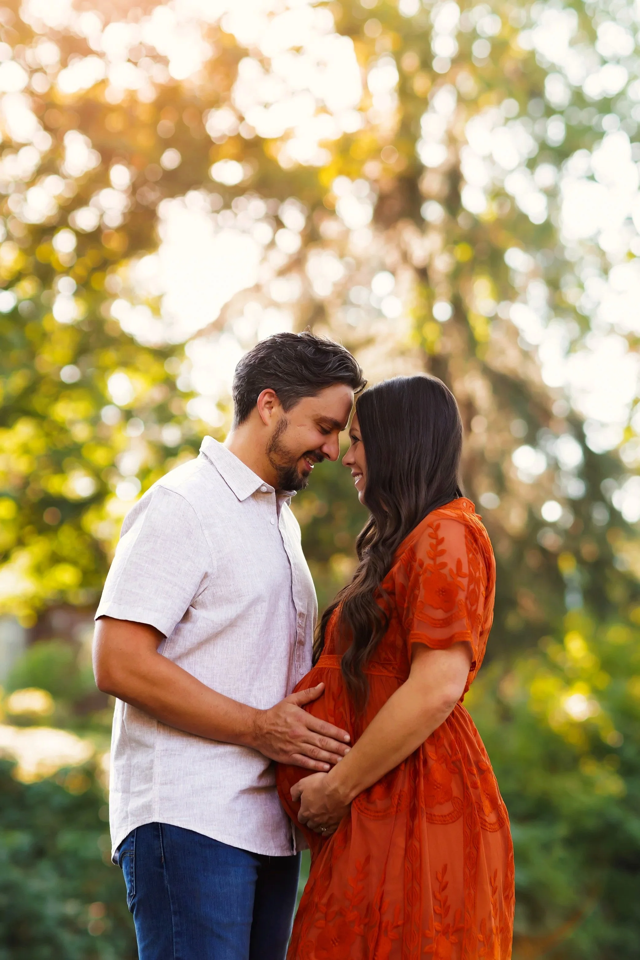 Expecting couple touching foreheads and holding baby bump during golden hour maternity session in Salem Oregon