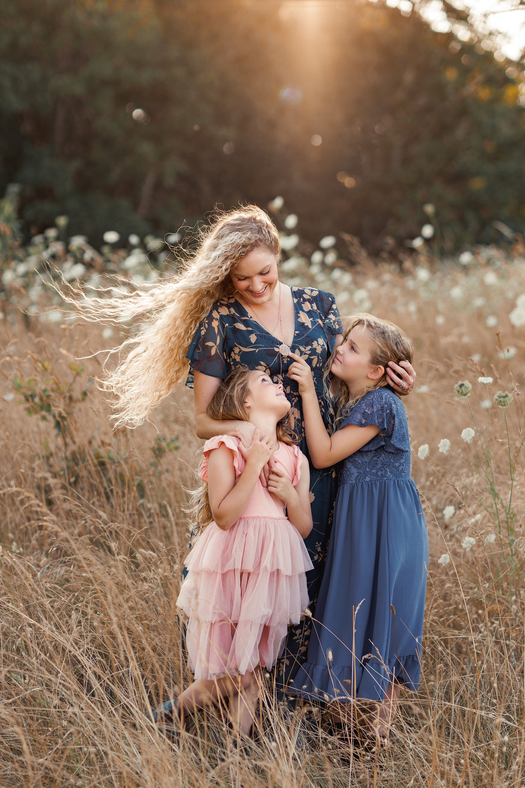 Mother standing in a golden field with two daughters hugging her and looking up at her.