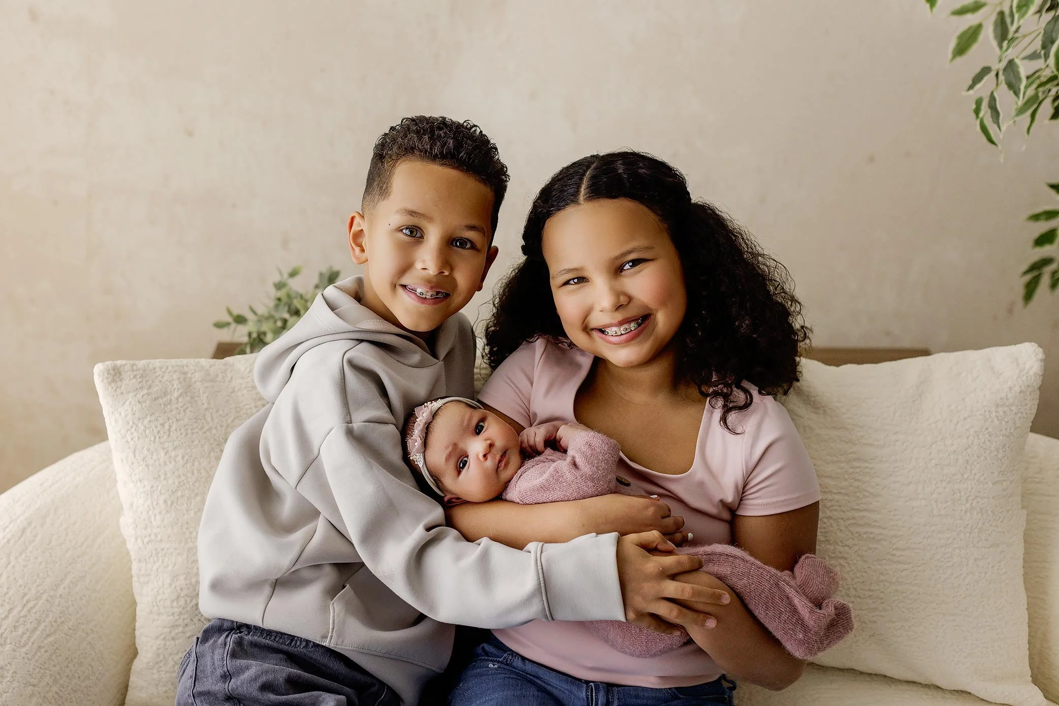 Young siblings smiling while holding newborn baby wrapped in soft blanket