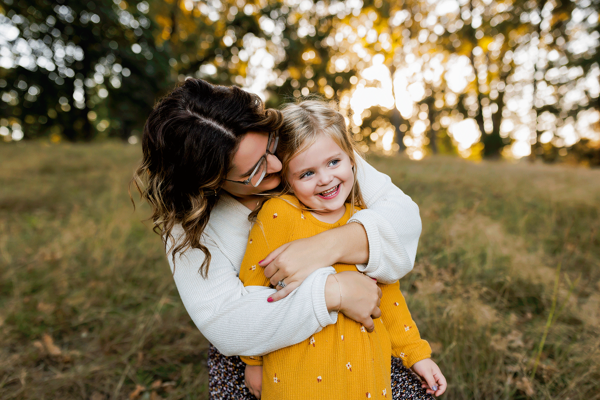 Mother embracing her smiling daughter in a yellow dress at sunset in Salem, Oregon.