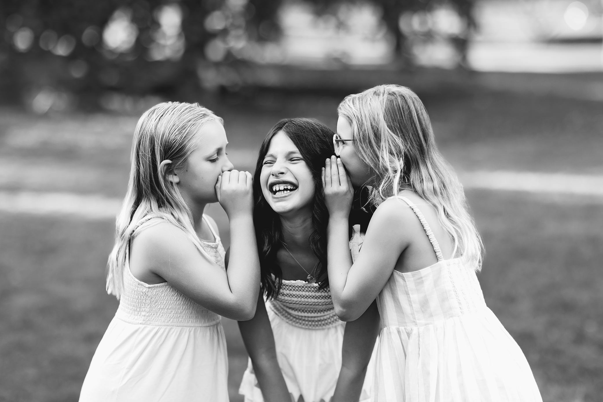 Three girls whispering to each other and laughing in black and white portrait