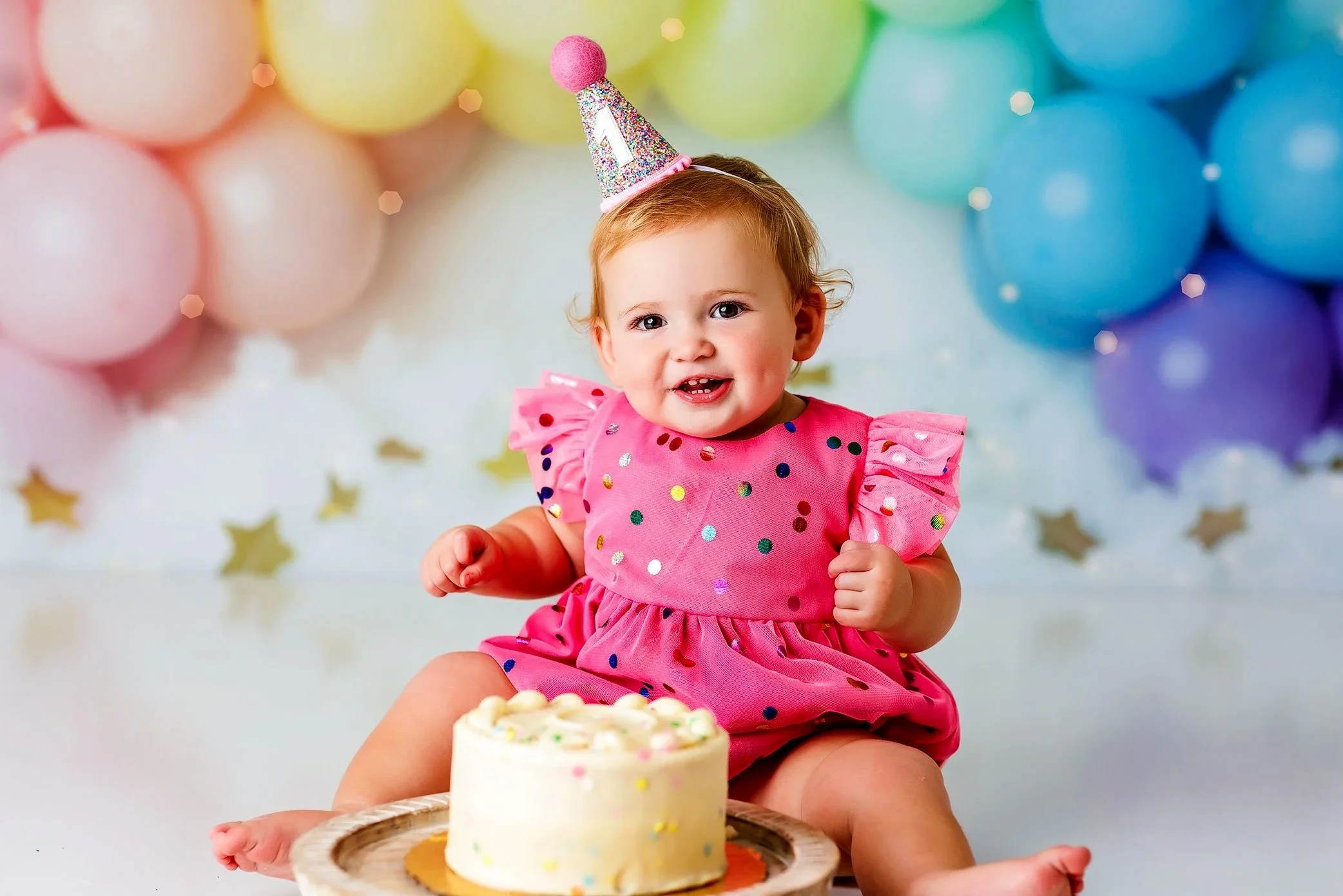 One year old baby girl celebrating with cake smash session, colorful balloons and joyful milestone photography
