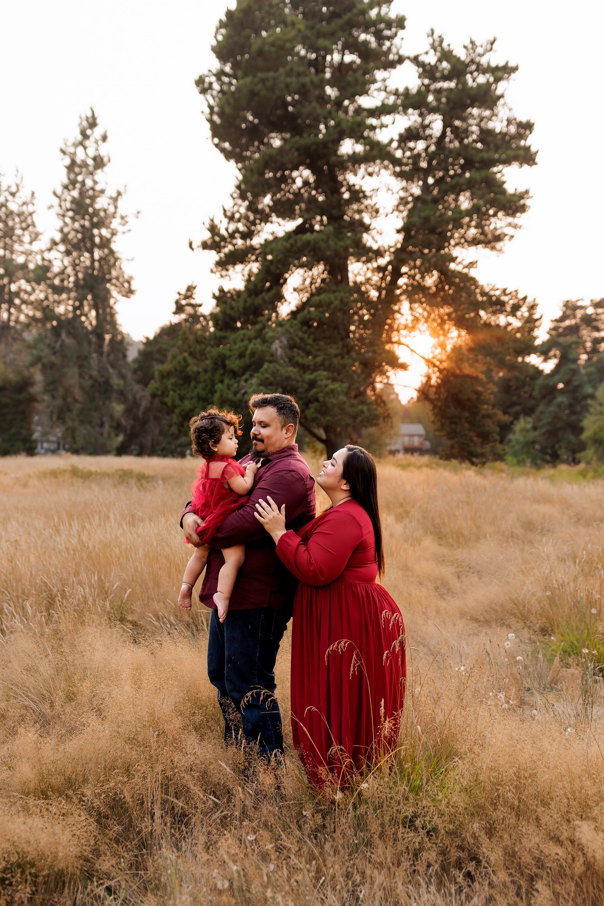 Mother hugging father from behind while he holds baby during golden hour family photography session in Salem Oregon field