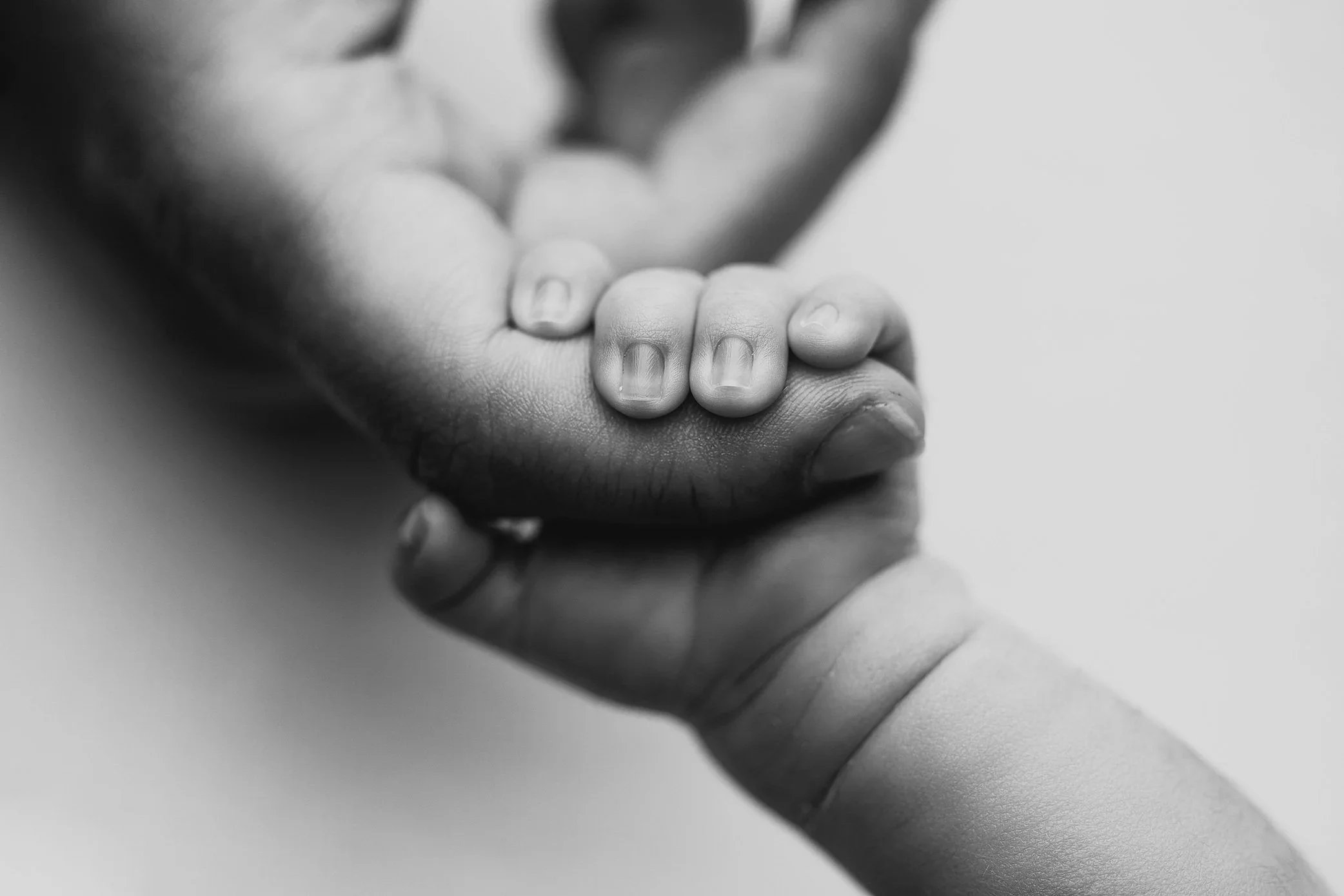 Newborn holding onto Dad's finger in Black and white.