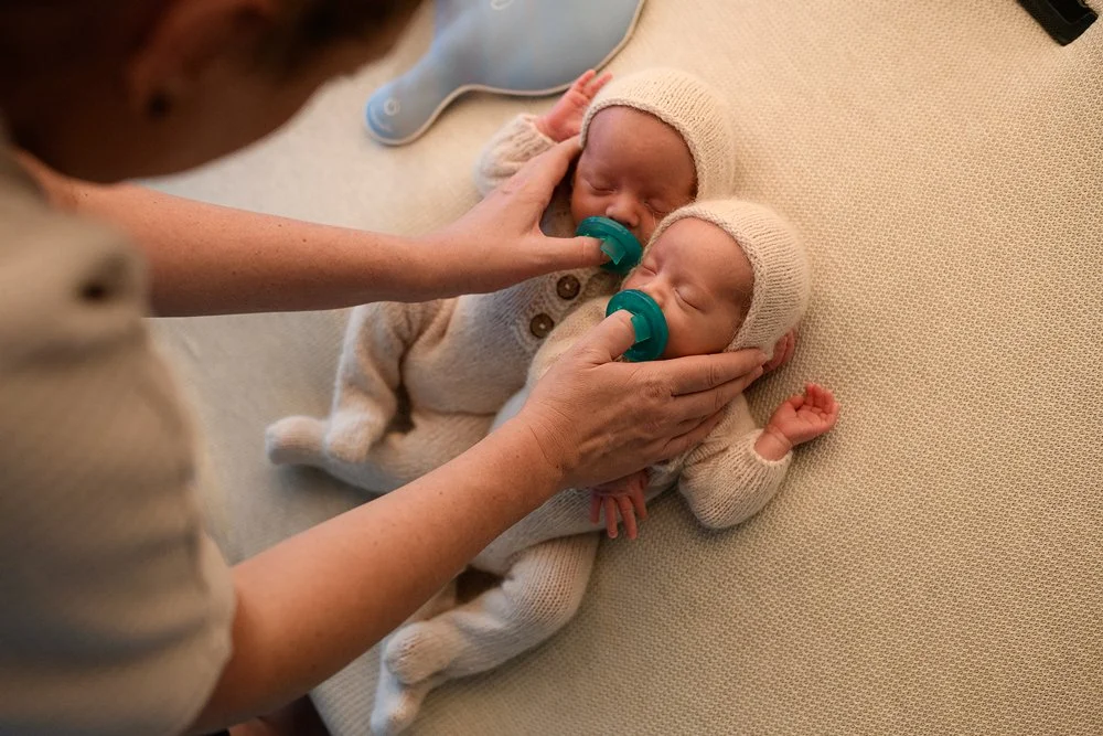 Newborn twin babies soothed with pacifiers by photographer hands during calm studio newborn session in Salem Oregon