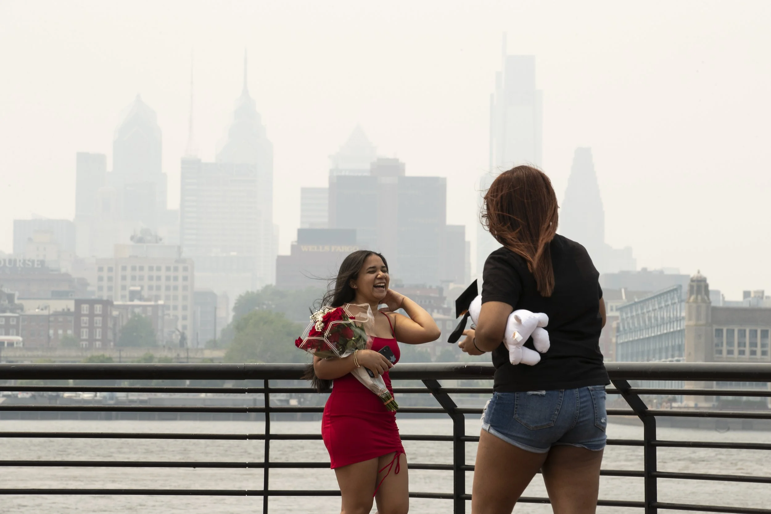  (left to right) Yirehliz Rivera, 14, laughs while taking 8th grade graduation photos with her cousin Julier Marquez as Canadian wildfire smoke obscures the Philadelphia skyline in Camden, NJ on Wednesday, June 7, 2023.  