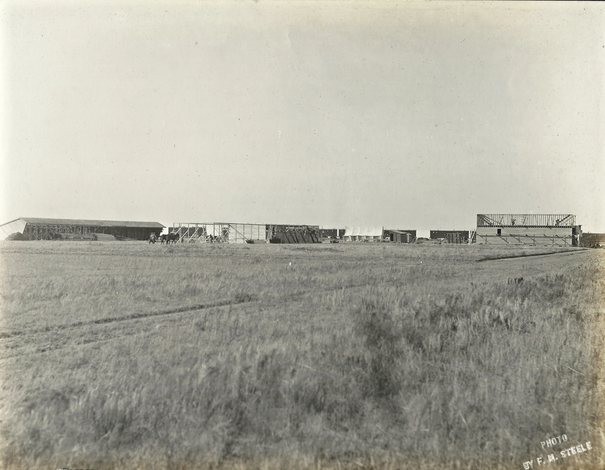 + Construction on the New Town, Sublette , 1912. In the background you will notice the rail cars in use on the newly laid track. The buffalo grass has been cut short to mark the new main street with construction on the first building in Sublette, The Cave Mercantile. This building for was known for many years as the T. M. Deal Lumber Company. There were living quarters upstairs which were used by the Cave family for a time; doctor Miner had an office upstairs also. The second story of the building was damaged in a storm and has since been removed. Construction has also begun on The Rounds & Porter Lumber Company, one block south of The Cave Store, they are preparing for the growth of the new county seat. The Rutledge tent were railroad crews were fed and housed can also be seen. 