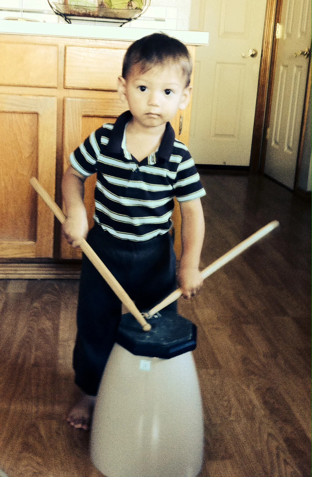 My son drumming on a drum pad and overturned trash can in the kitchen