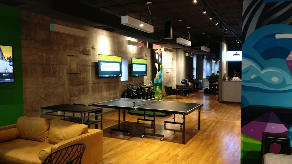 FIVE IRON GOLF - 2017 We transformed this Flatiron former yoga studio into a golf simulator lounge. Four room-sized virtual driving ranges form the backbone of the space. In between we added a reception area and lounge, a few putting greens, and a bar and kitchen. Finishing touches include custom painted murals and faux-exposed concrete walls to give an urban contrast to the pastoral courses projected in the simulators.