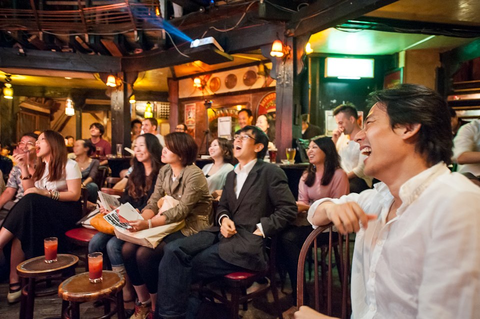 Mixed Japanese and international audience laughing at an English and Japanese improv comedy show in Tokyo