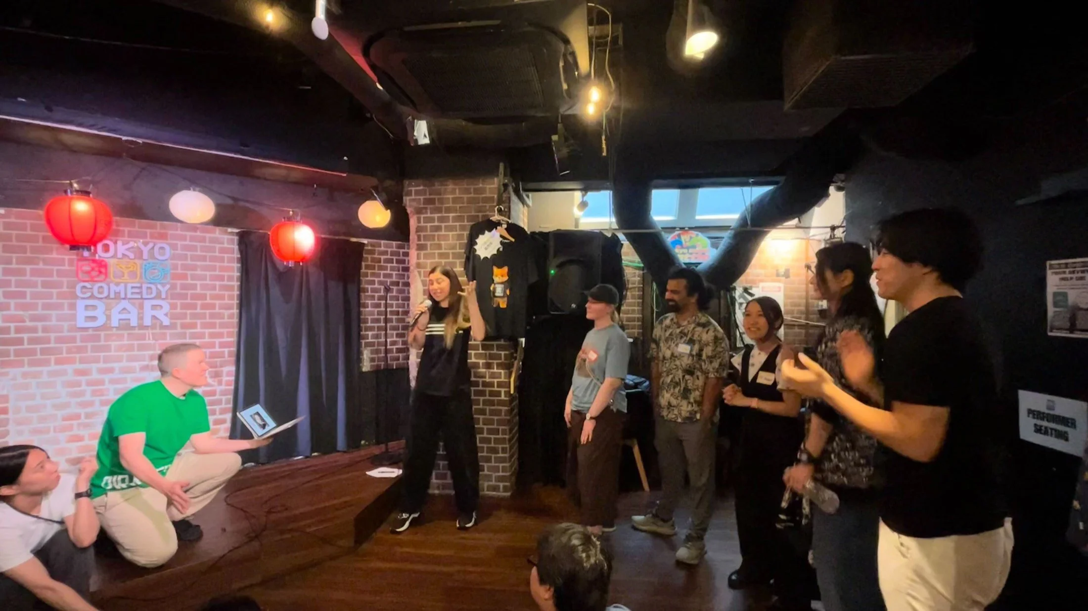 Tokyo Comedy Barでのパイレーツ・オブ・東京湾のオーディションで、マイクを持ちキツネのTシャツを掲げる司会者。
