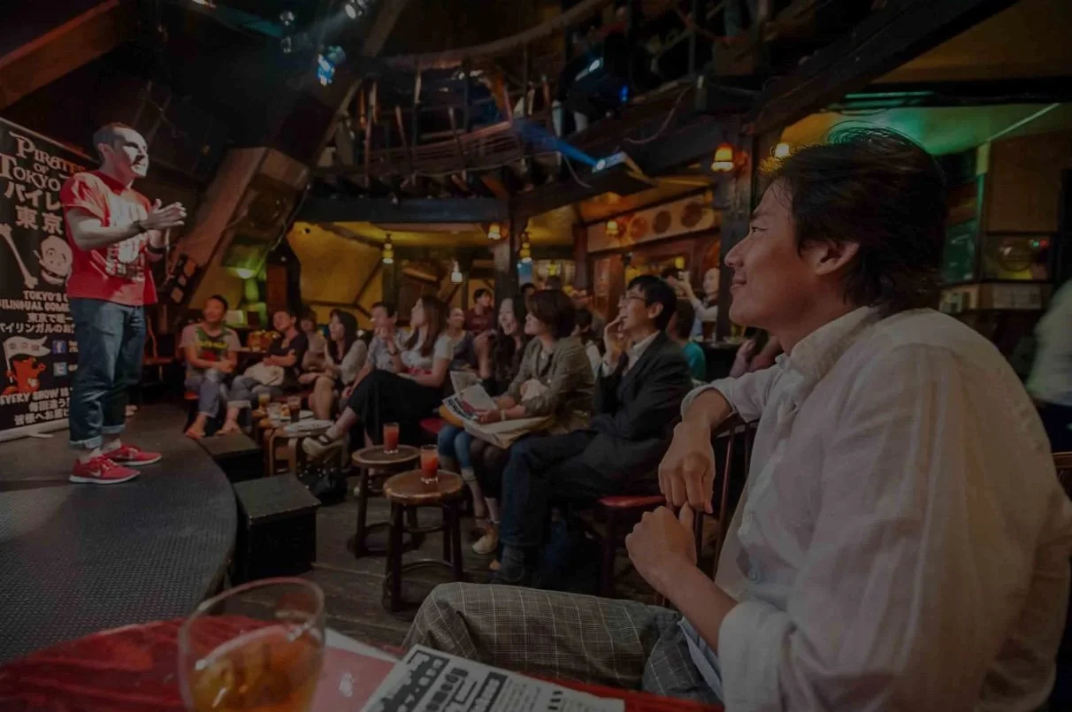 恵比寿のブリティッシュパブ「What the Dickens」での即興コメディライブの様子。多国籍な観客と一緒に盛り上がるステージ。 | Pirates of Tokyo Bay improv comedy performer on stage at What the Dickens in Ebisu engaging with a multicultural audience.