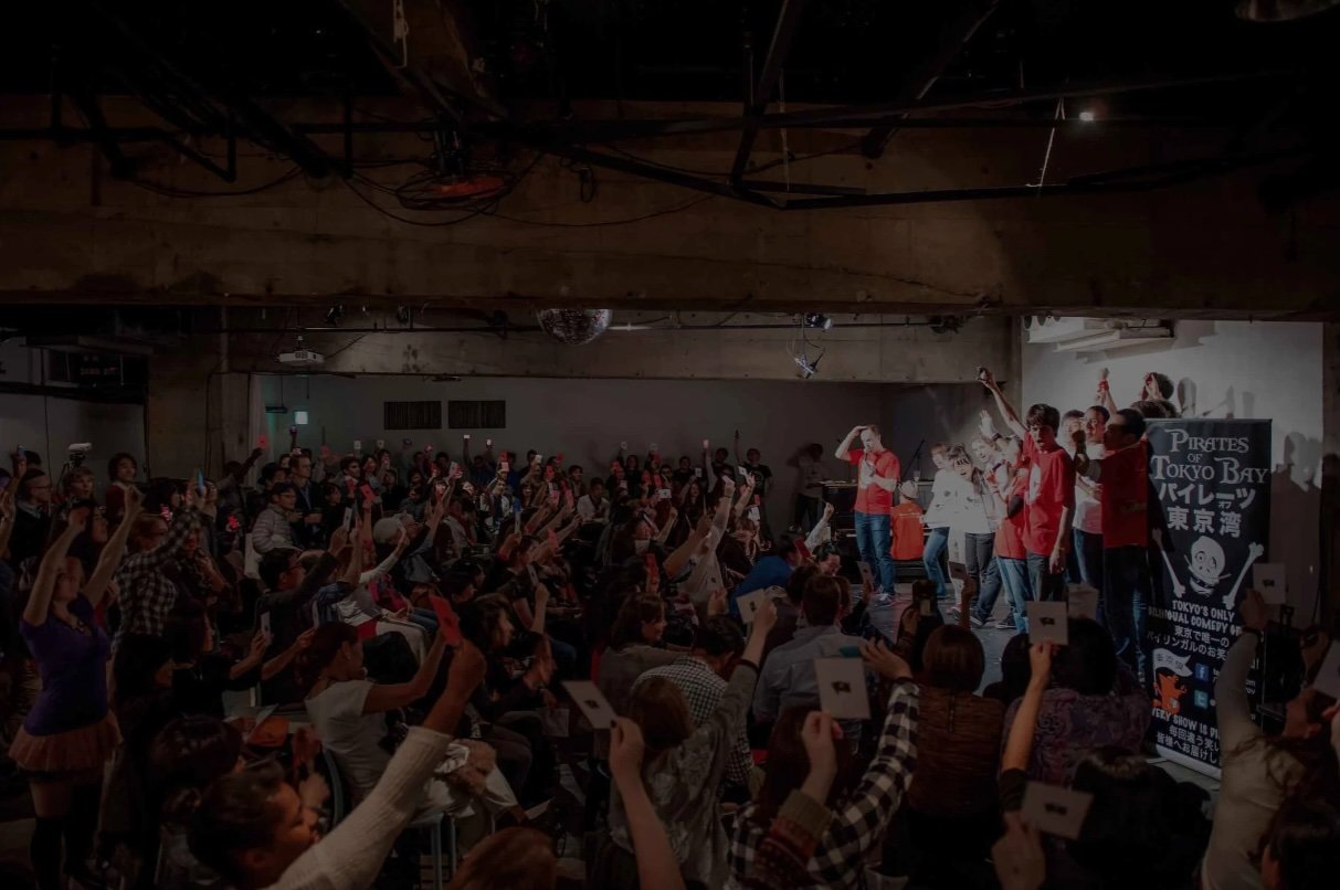 六本木でのスペシャルアニバーサリーライブ。ステージ上で日本語と英語の即興コントを披露するメンバーたち。 | Pirates of Tokyo Bay members performing on stage to a large crowd at a special anniversary event in Roppongi.