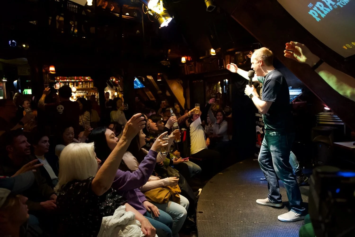 Performer and audience raising a kanpai toast at an improv comedy show at What the Dickens! in Ebisu Tokyo | 忘年会 乾杯 即興コメディ 恵比寿 | Pirates of Tokyo Bay
