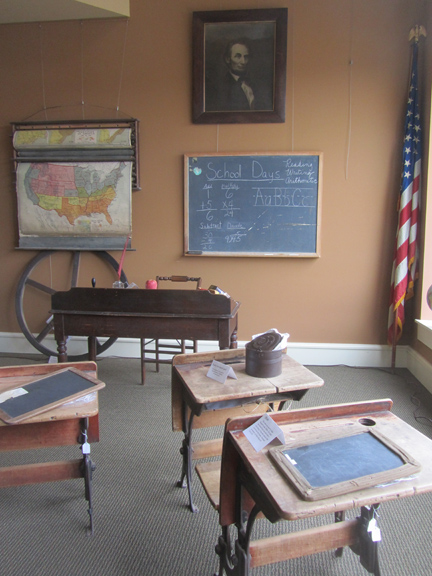  This museum gallery exhibit represents an early Lawrence County schoolroom. The wheel came from the bell tower at Central School. The maps were from the Springville School. At the beginning of the day, students recited the pledge of allegiance in fr