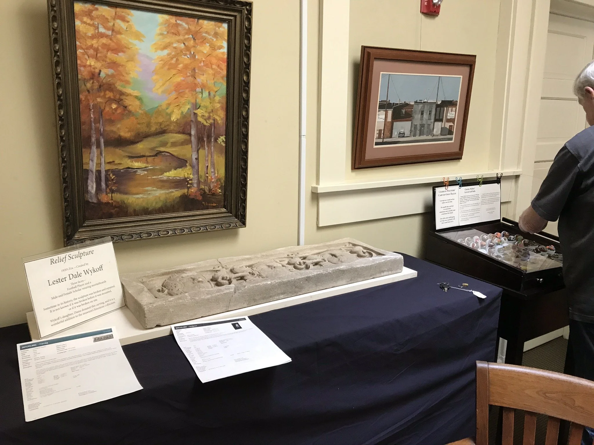  Fall scene by former LCCAA member, Elizabeth Vaught, Lester Dale Wykoff limestone relief sculpture, Charles Walters’ carved golf balls in the case at right.  
