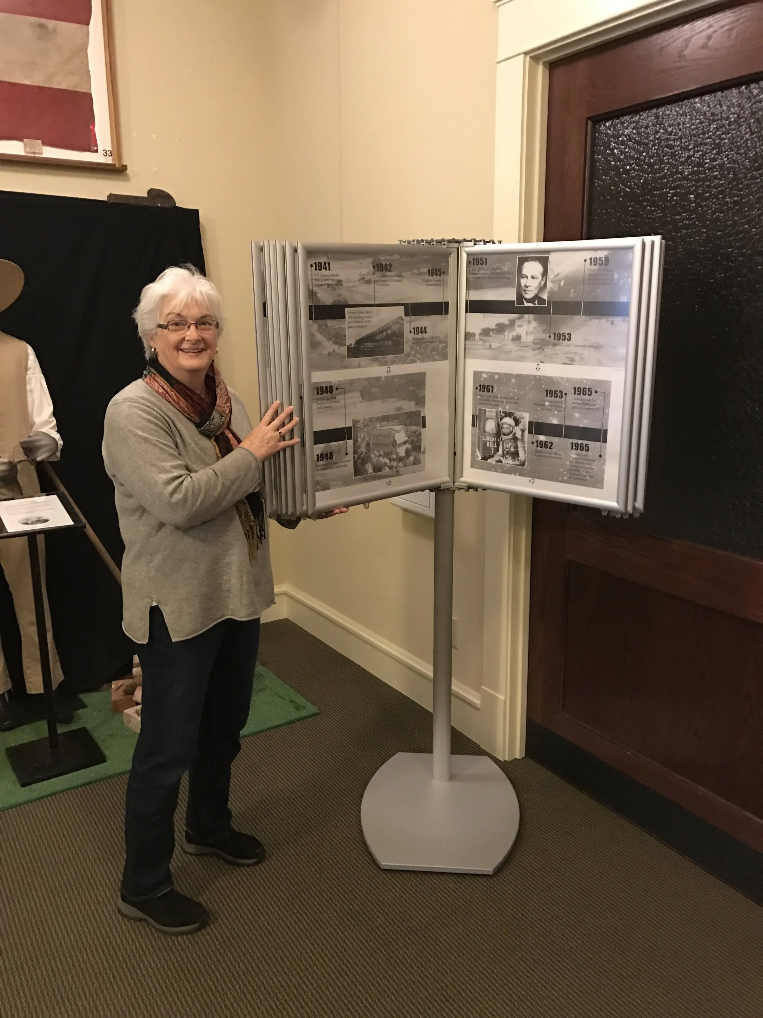  Becky Buher is standing by small copies of the complete set of murals , which are on display in the gallery. 