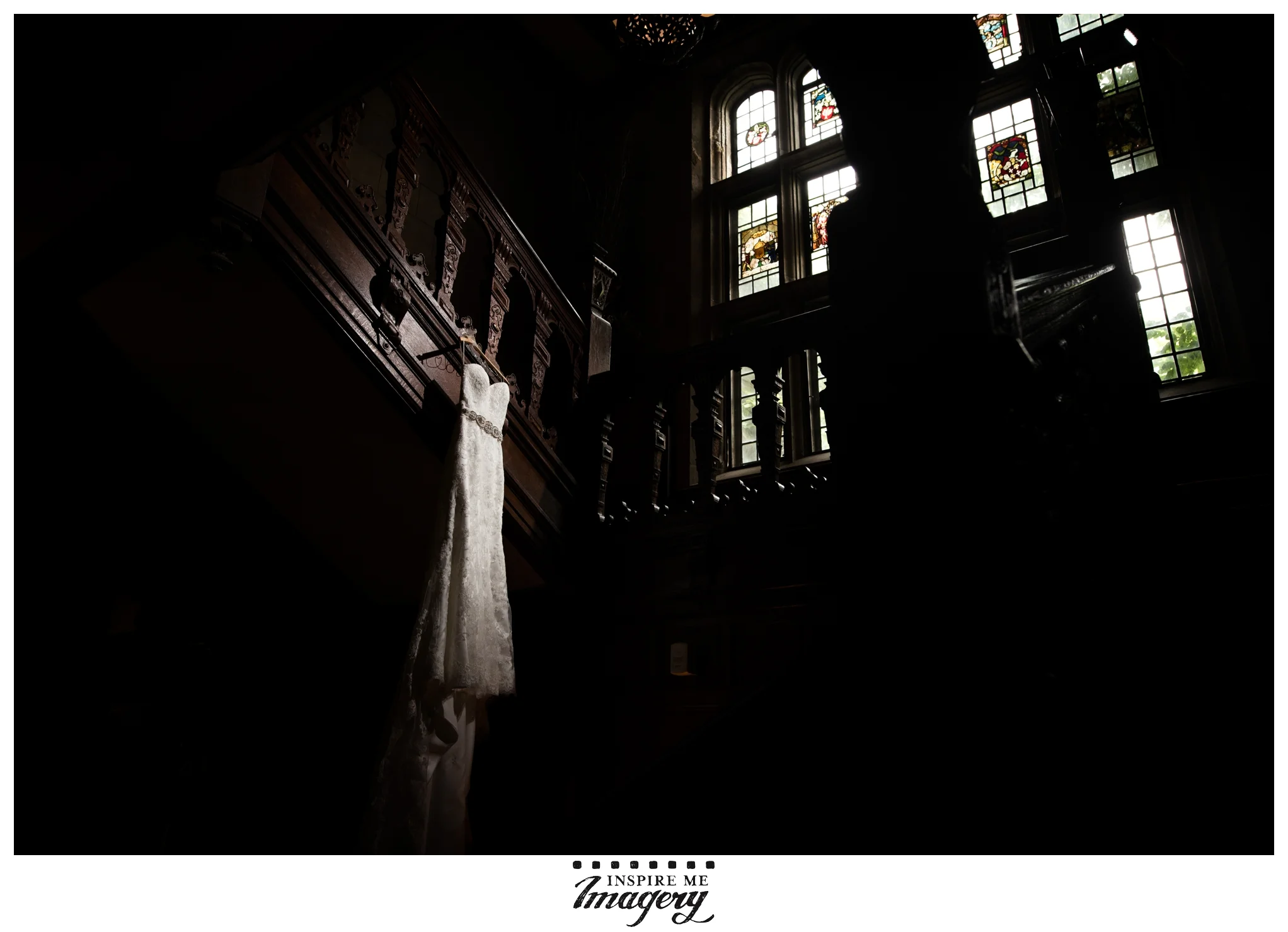 The dark wood of the staircase and bannister are a beautiful contrast to her white dress, and the gorgeous stained glass windows can be seen in the background.