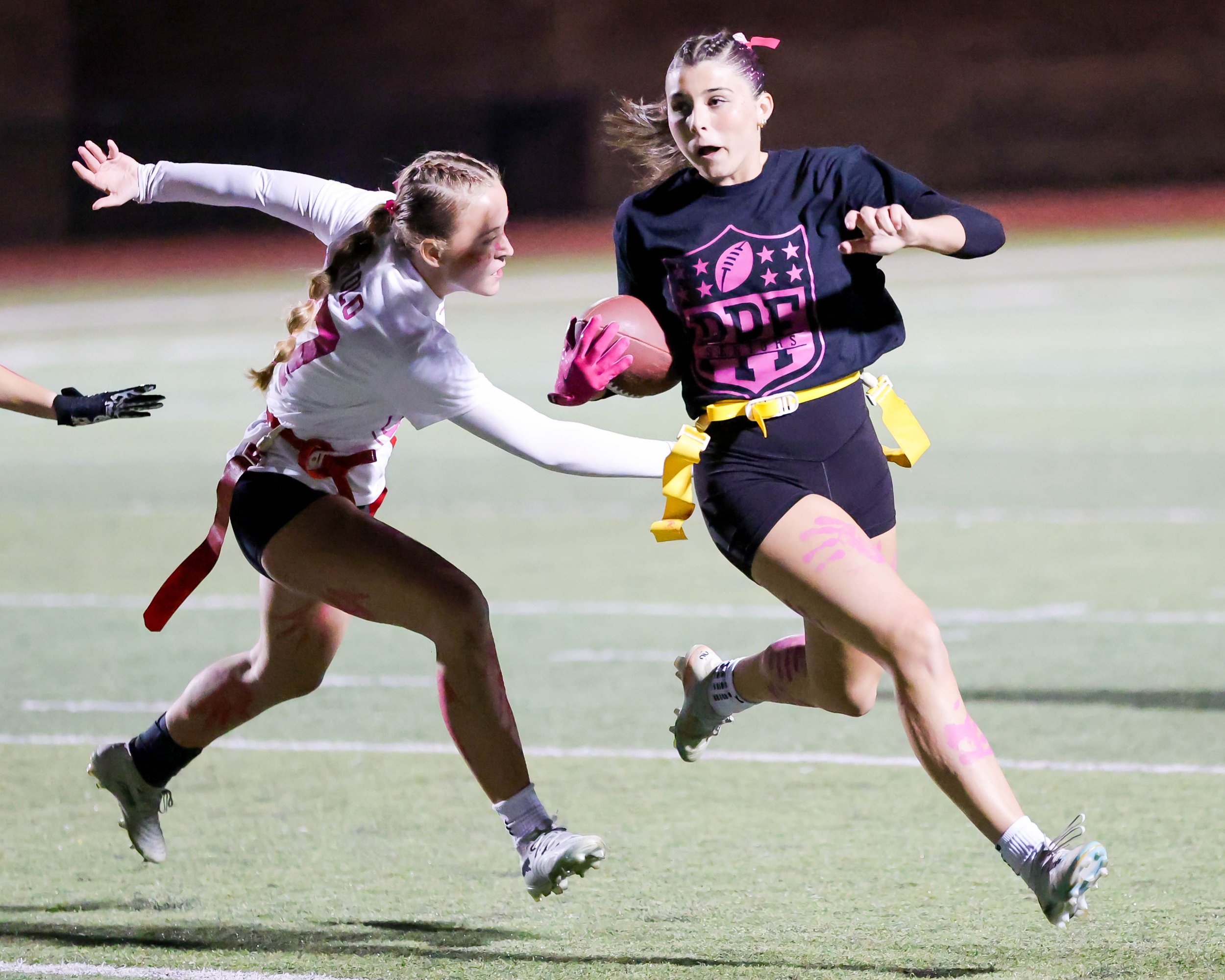 Senior running the ball with a Junior grabbing the her flag