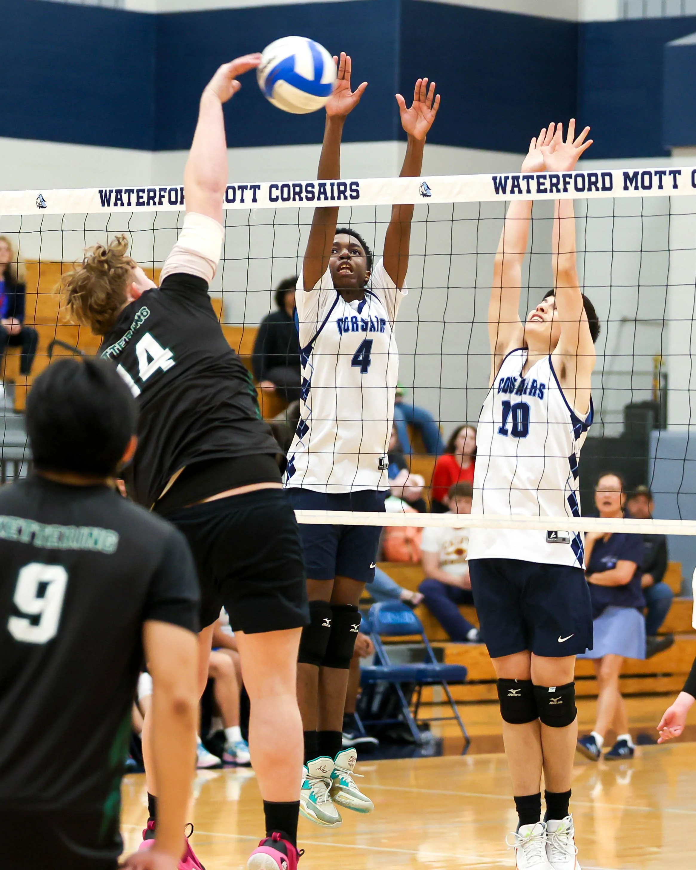 Kettering #14 spikes the ball with Mott #4 and #10 try to block it