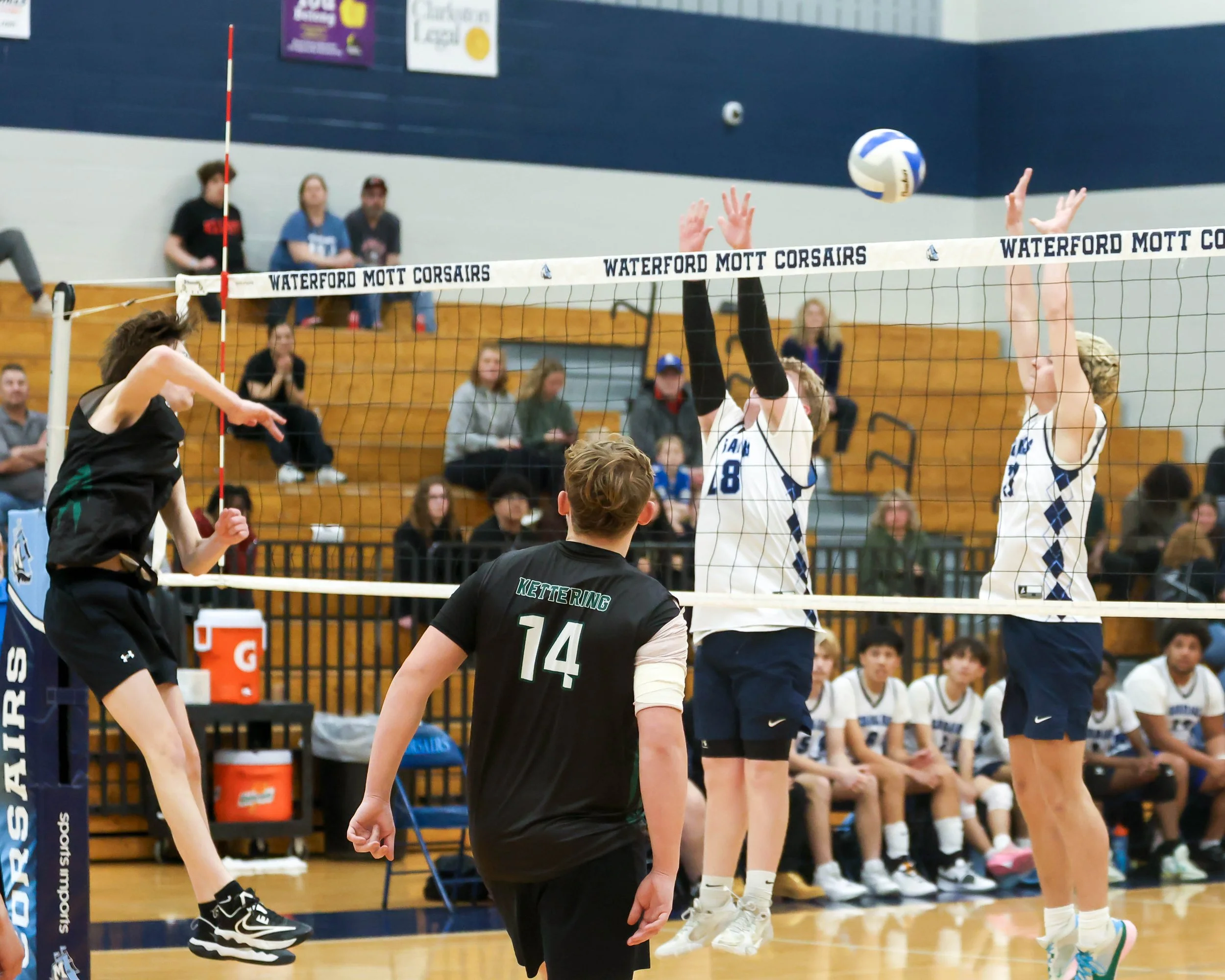 Kettering #12 spikes the ball and Mott #18 and #12 try to block the ball