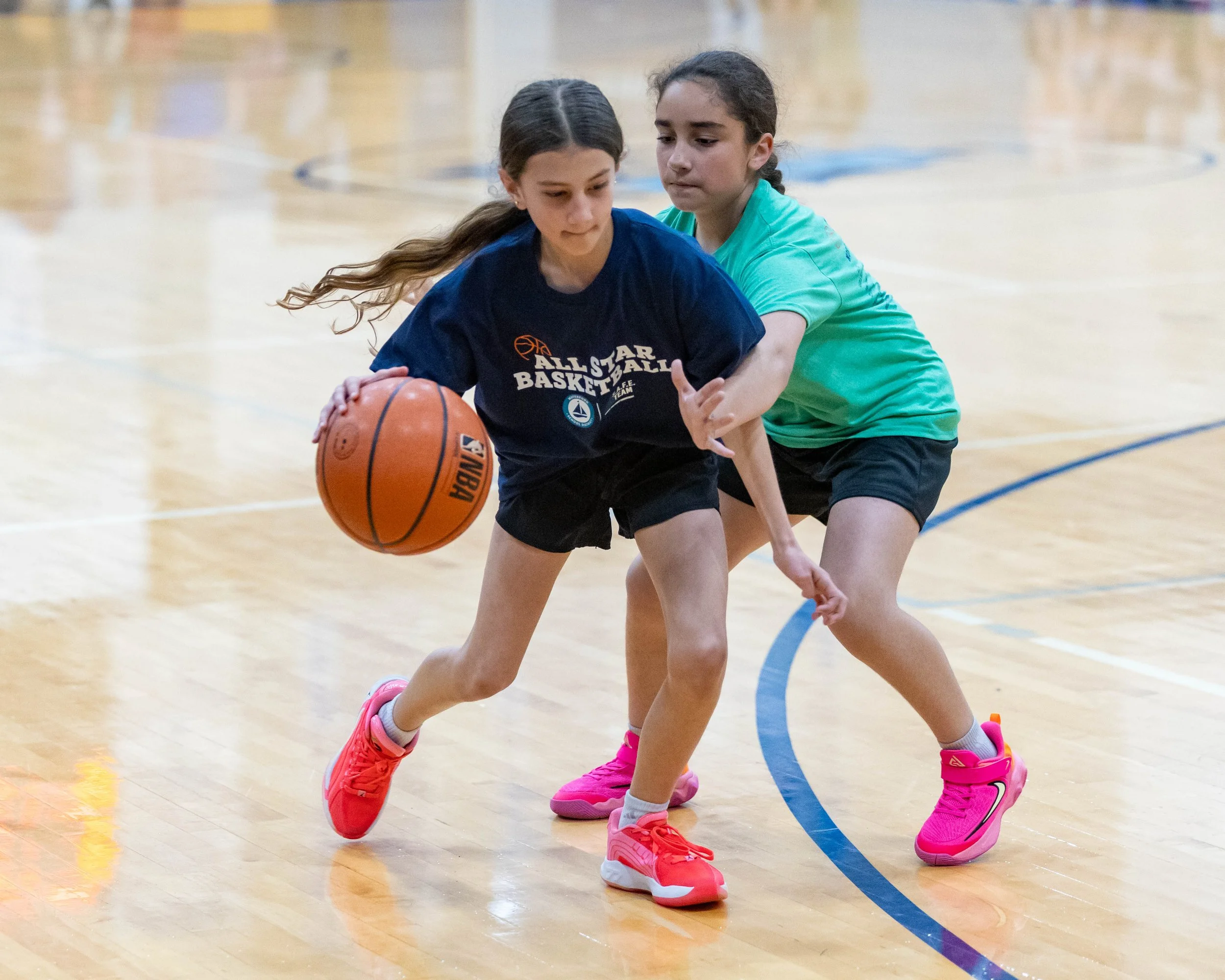 North girl dribbles the ball guarded by South girl