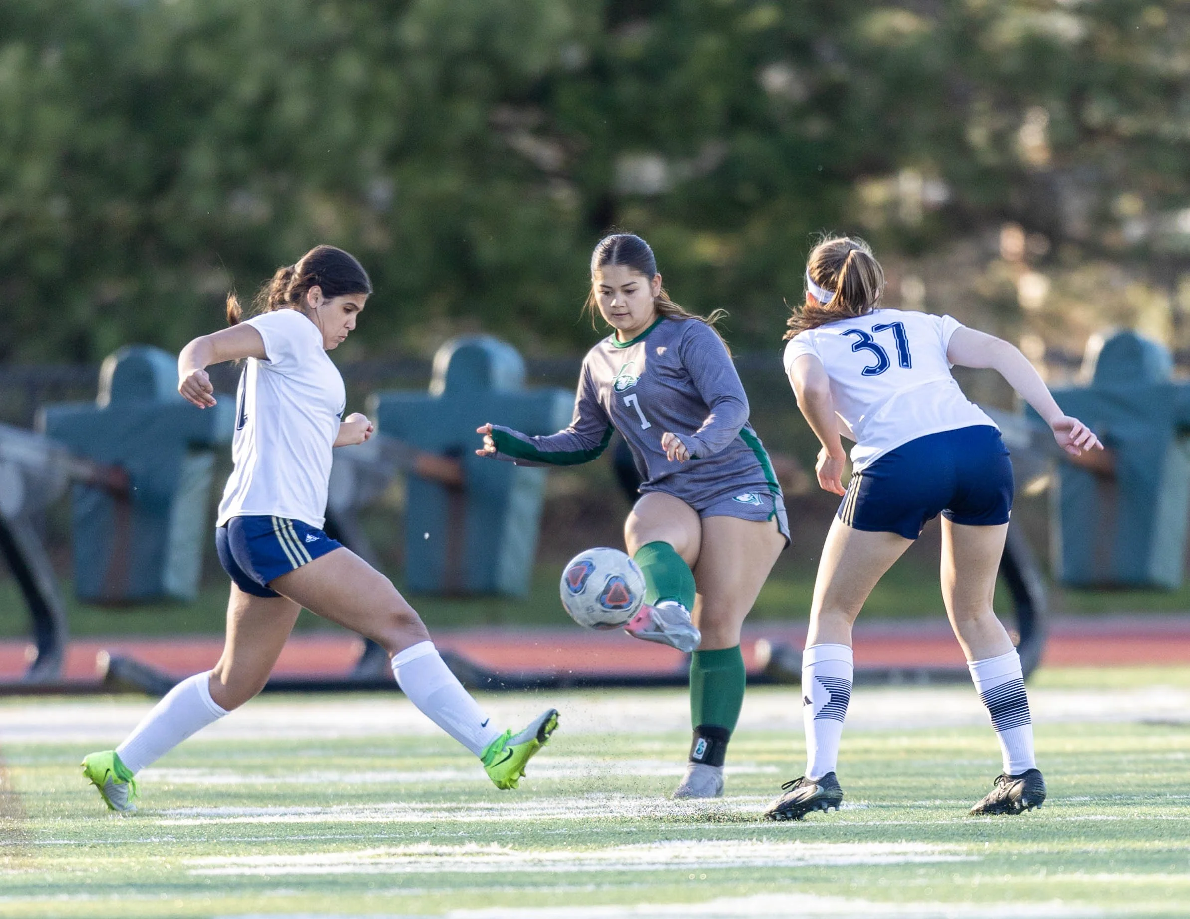 #7 kicks the ball with two DCC player near her
