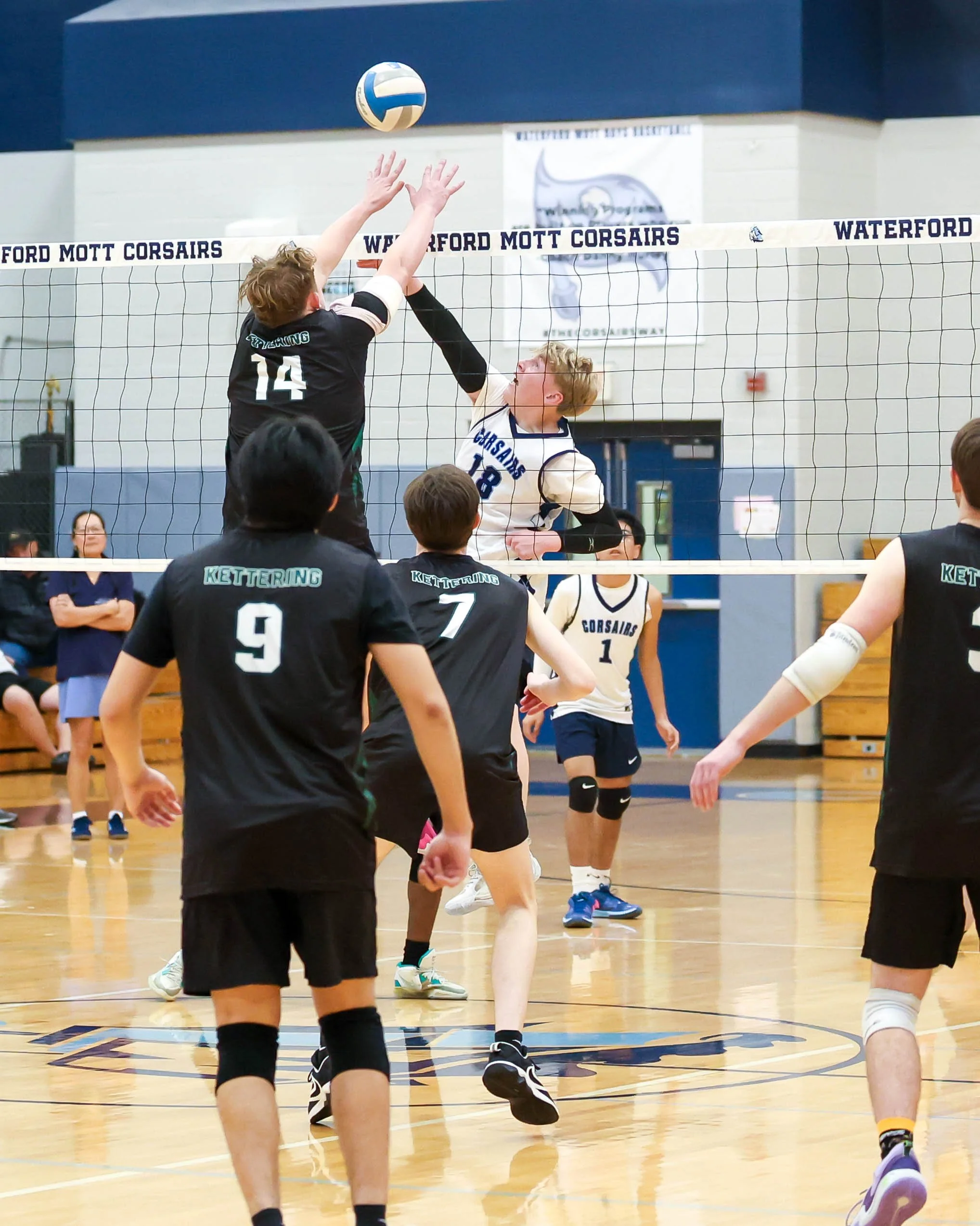 Mott #18 hits the ball and Kettering #14 tries to block it