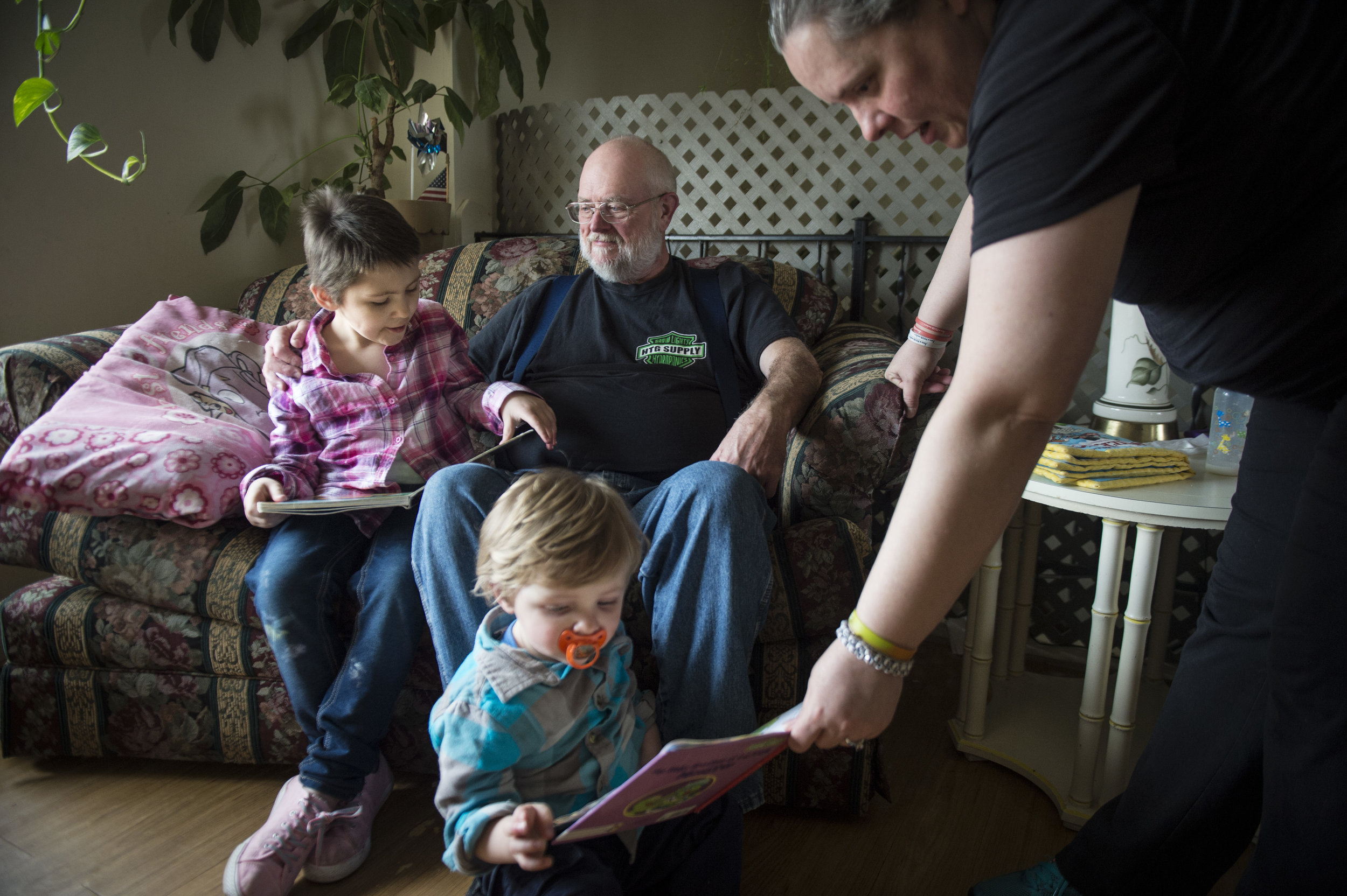  Naomi sits on a the couch with her grandpa and reads him a book while Donna hands her son Kenny, 2, a book. &nbsp; 