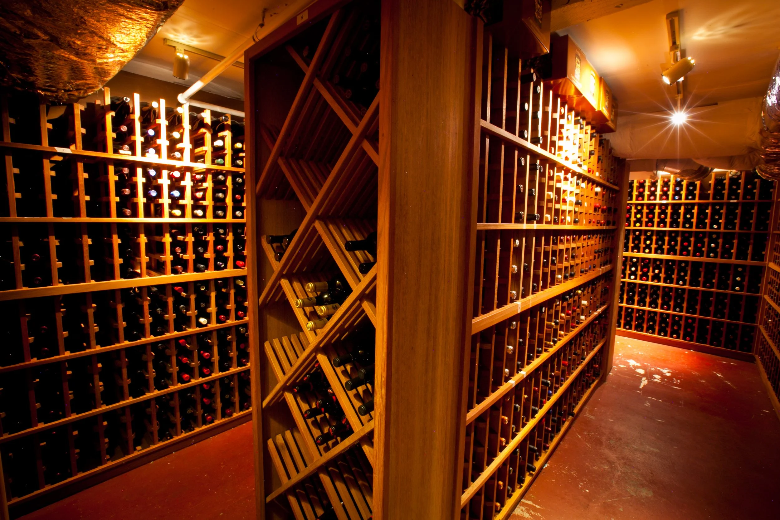 Wine cellar with wooden racks filled with wine bottles, dim lighting, and a warm ambiance.