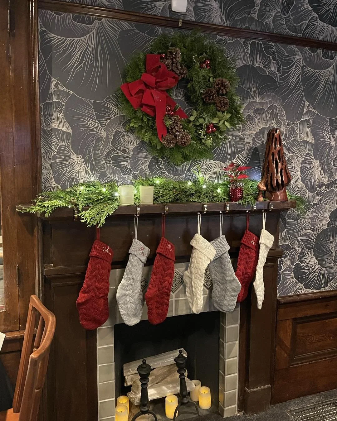 Christmas decorated fireplace mantel with stockings, candles, and greenery, with a wreath above.