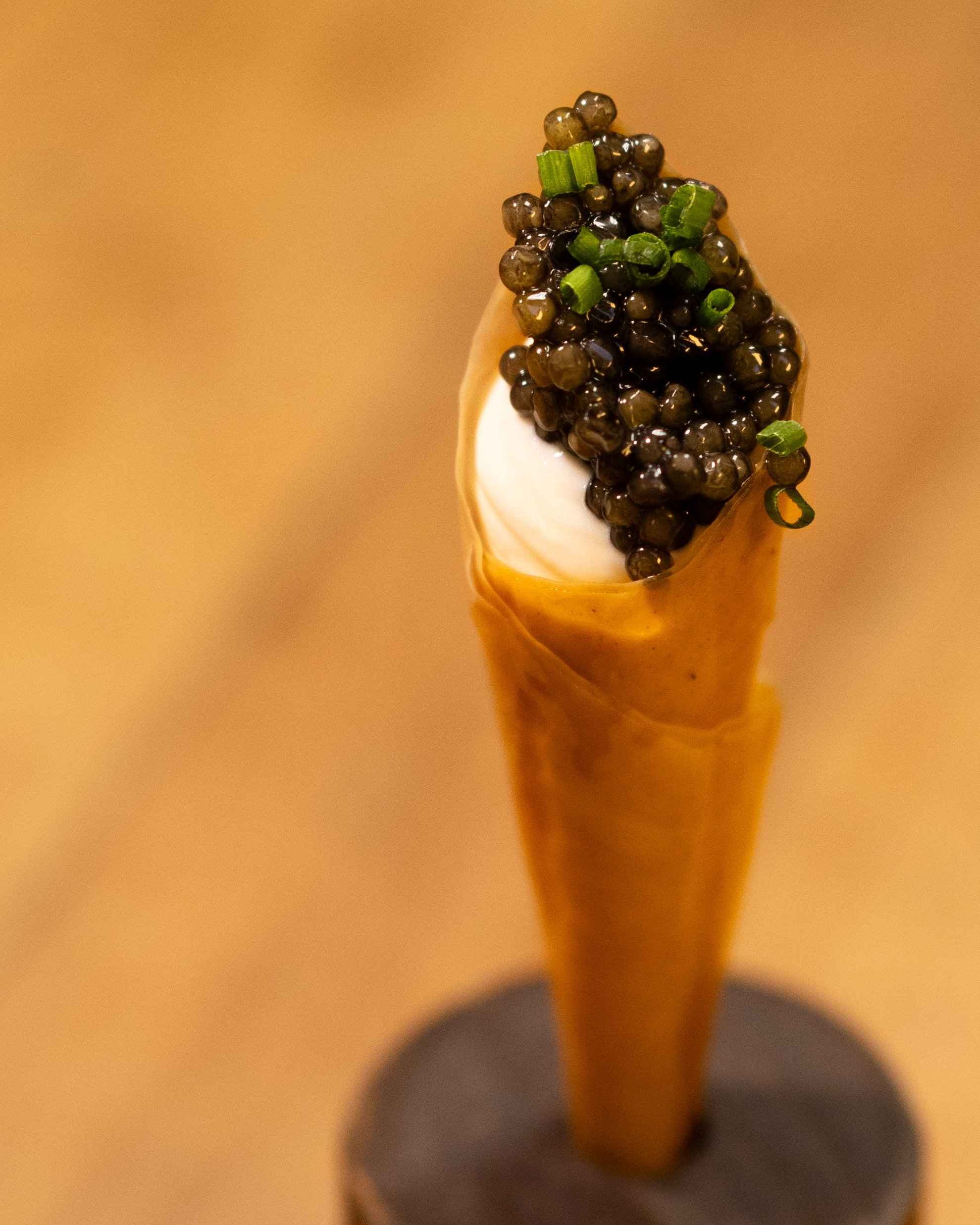 A cone filled with creamy white and brown topping, garnished with black caviar and chopped green onions.