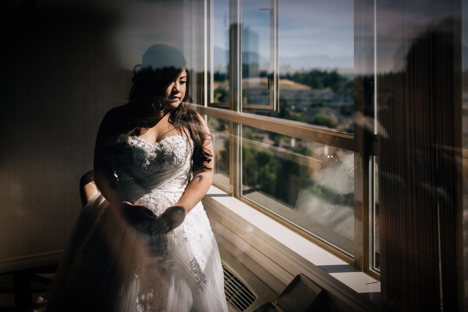 asian bride looking out sandman hotel window for wedding in surrey