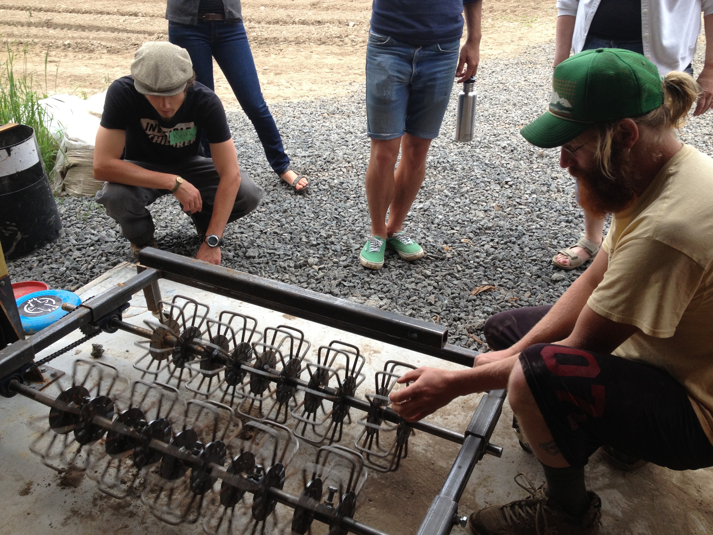  Ryan, the farm's mechanic (far right) shows off the basket weeder he made recently. It fits on the bottom of their cultivating tractor and enables them to plant their spinach and salad mix in non-standard 4-row beds. 