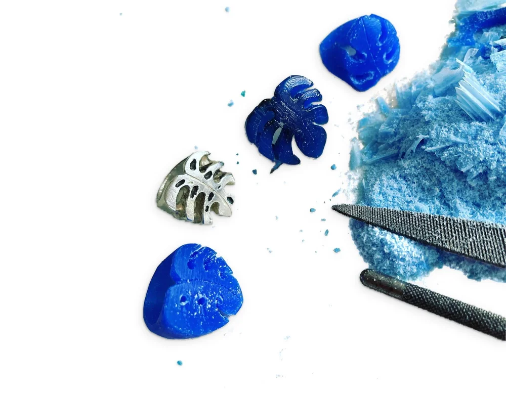 Hand-carved blue wax Monstera rings beside the finished sterling silver Monstera Ring, with carving files and wax shavings
