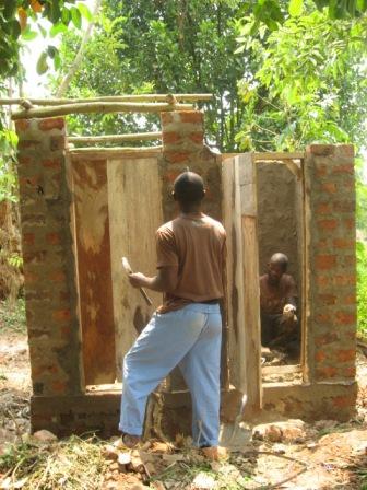 Francis Lubega and his apprentice work on the forms for the roof for his neighbor's new toilet. 