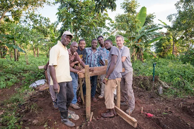 The men pose proudly near their newly constructed stand, ready to position the water tank for the drip irrigation system.