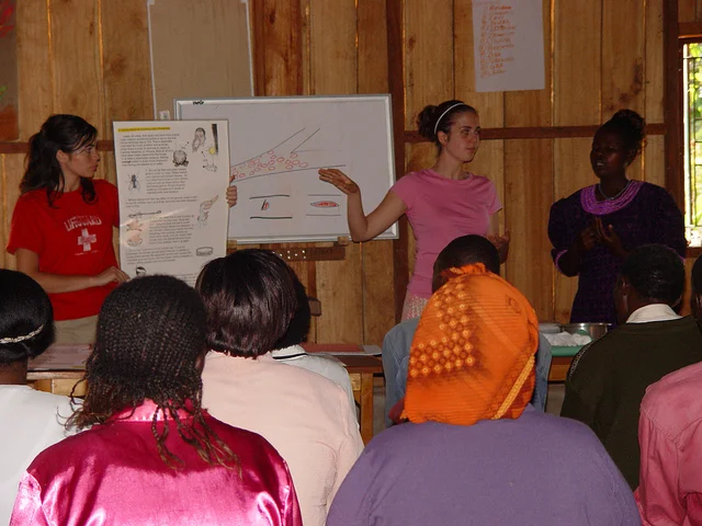 Heather Munoz (left) and Celesta Bargatze (right) teach a room full of Kenyan women about the importance of nutrition, and what preventative measures they can take to protect their households from diseases like malaria (2005). 