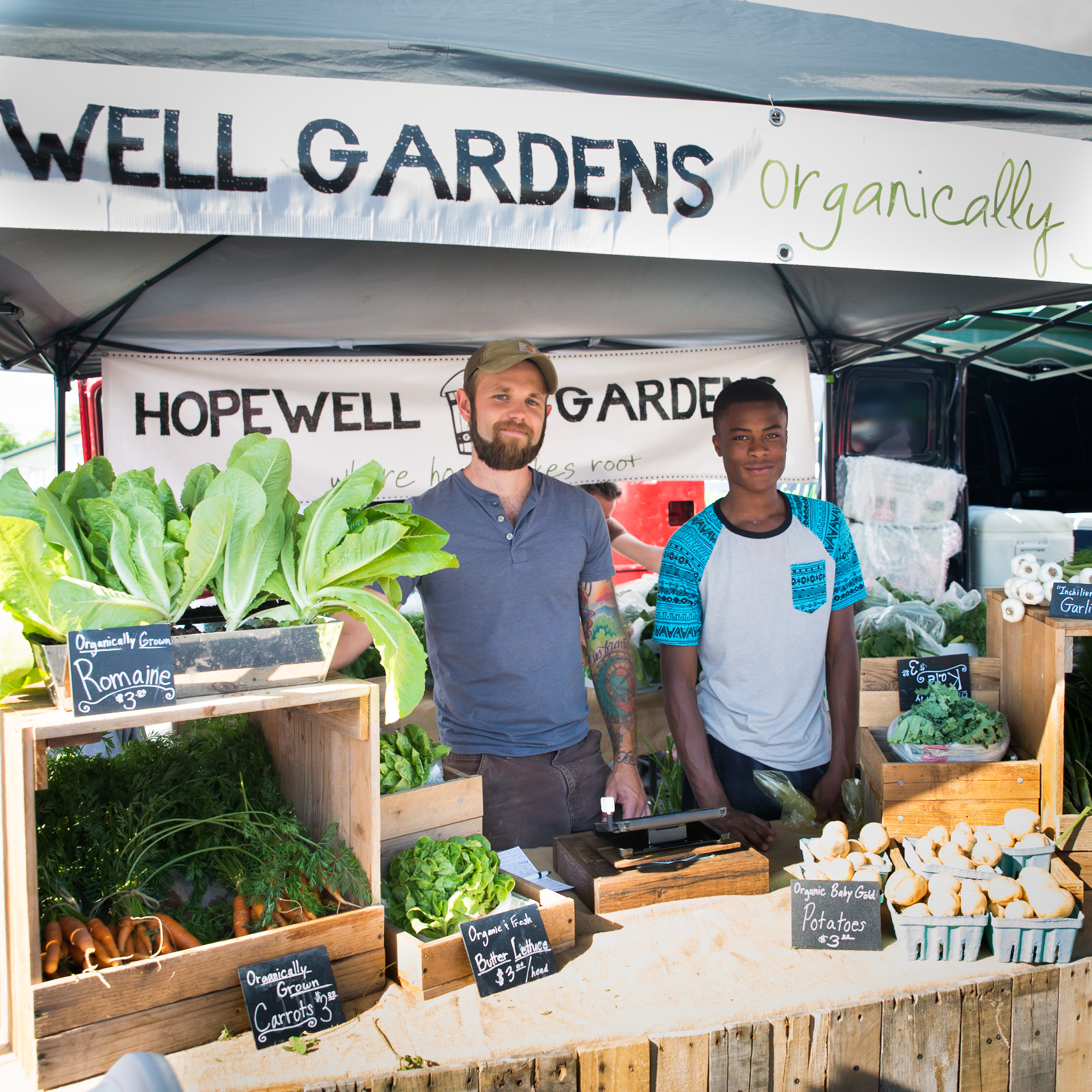 Geoff Hartnell is assisted by Gerron, a friend and neighbor, at the local farmer's market. Gerron was inspired after learning gardening at Camp Skillz, and created his own garden for his family in his backyard. 