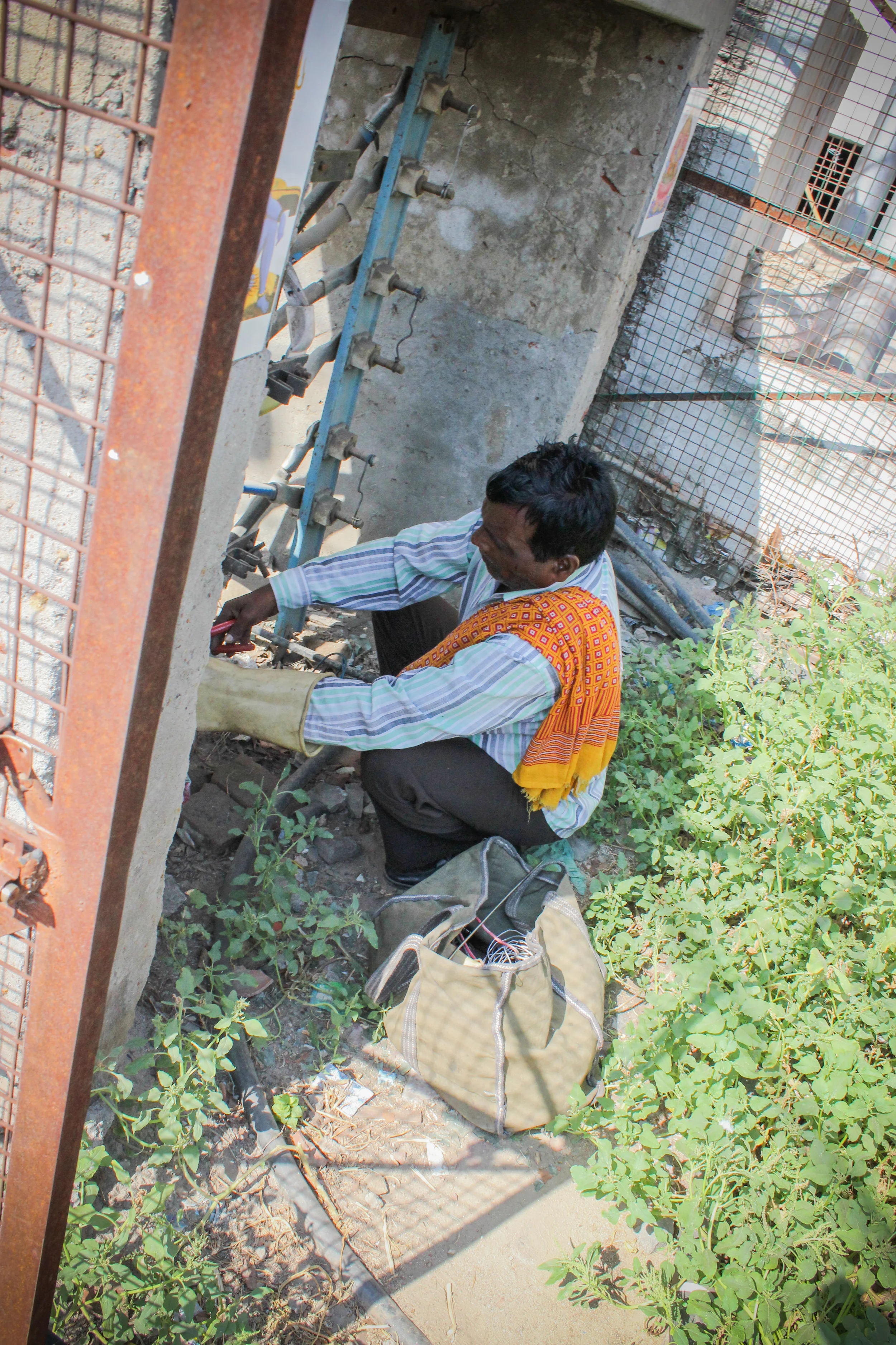 Utility employees face equally dangerous conditions, servicing power stations with inadequate tools and limited technical knowledge. This serviceman repairs a large power relay with nothing more than a glove for protection and a cloth bag of basic tools.