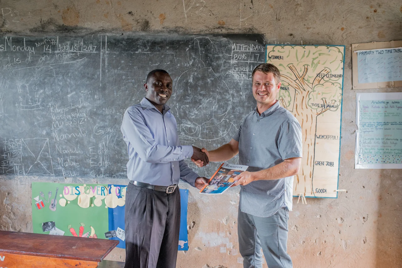 Cameron Kagay, G.O.D. East Africa's Lead Manager, delivers Resources Magazine to the head teacher at St. John's Primary, Lawrence Ssemakula (writer of this article). 