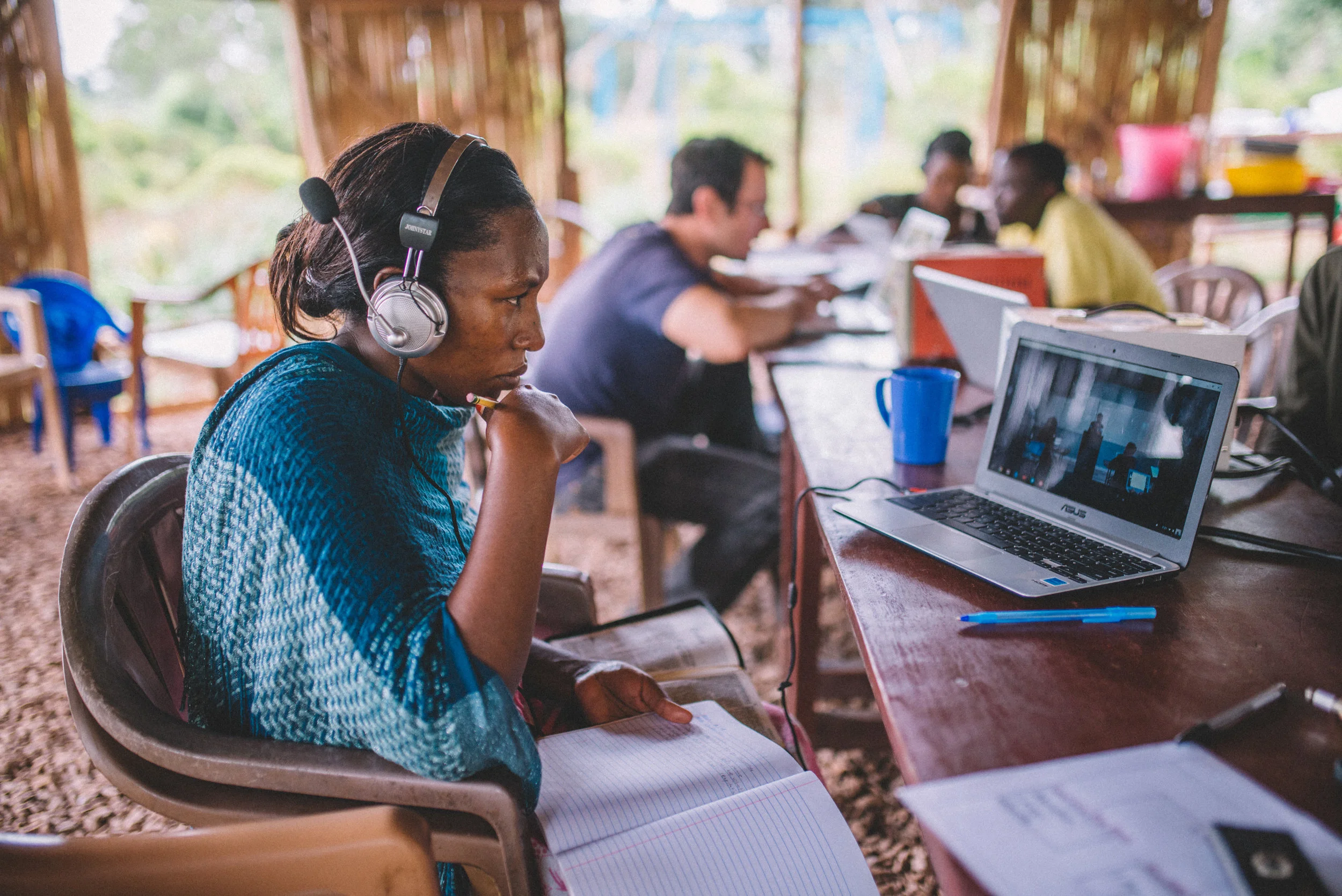 Annette Nabugo tunes in to her cooperative Bible class "Biblical Foundations for Ministry," recorded at the Institute for G.O.D. and made available via the internet to her home in rural Uganda. Behind her, Brandon Galford, a Bible teacher, meets with other students to review the material. 