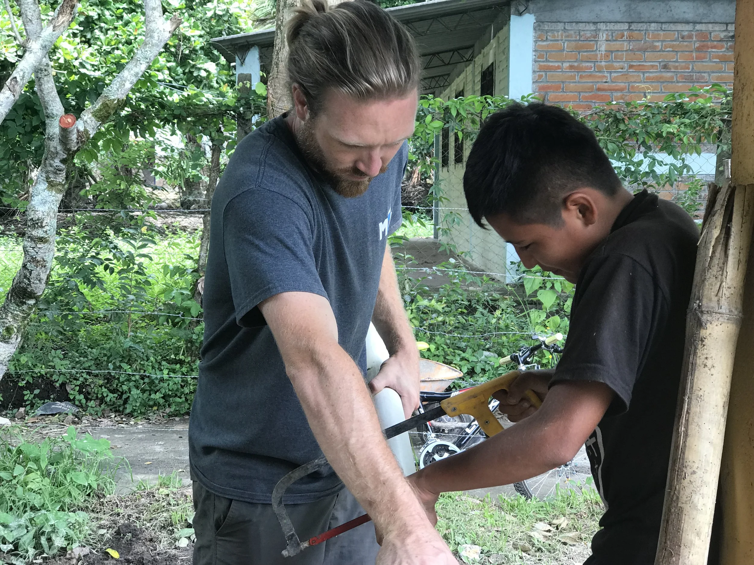 Kyle taught their 12-year-old neighbor, Augustine, how to cut PVC pipe to connect it to the plumbing line of the bathroom. 