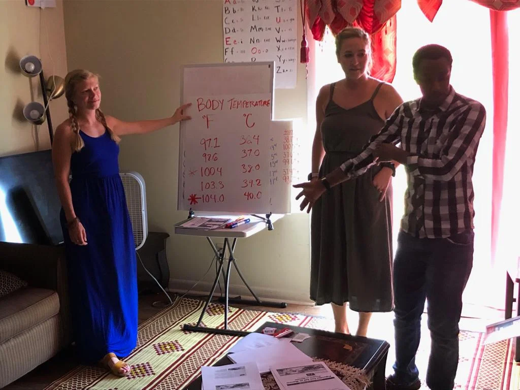 Christina James and Jordan Miller, both medical assistants and members of the G.O.D. East Africa team, teach Congolese refugees how to tell temperature in preparation to read thermometers for the first time.