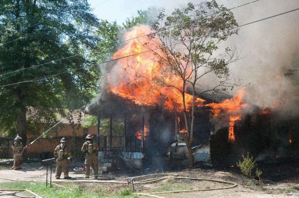 Firefighters spraying water on a house engulfed in flames and thick smoke.