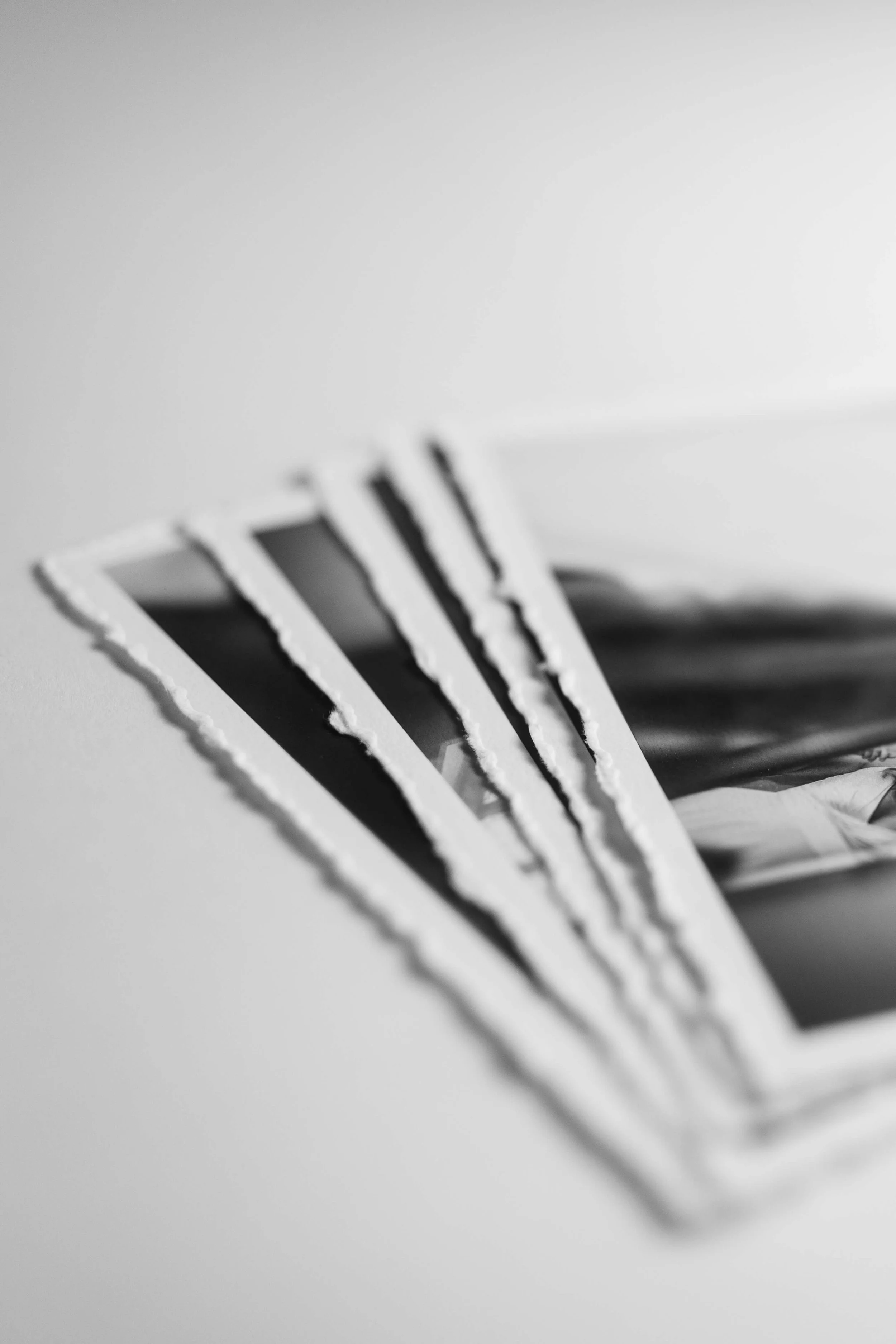 Stack of black and white photographs with torn edges, arranged on a white surface, with some shadows.