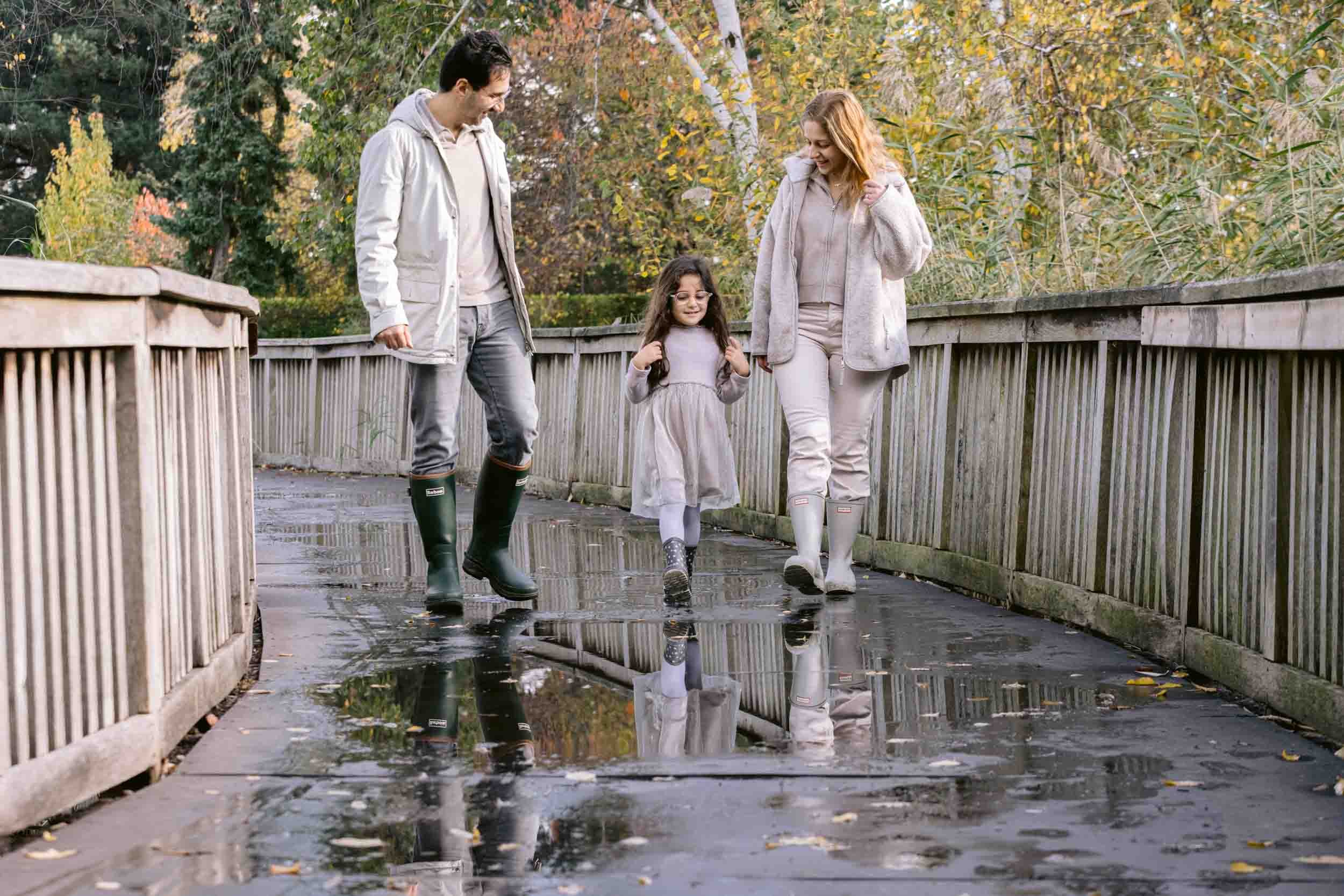 Family walk over the bridge in Regent's park with their reflection in puddle
