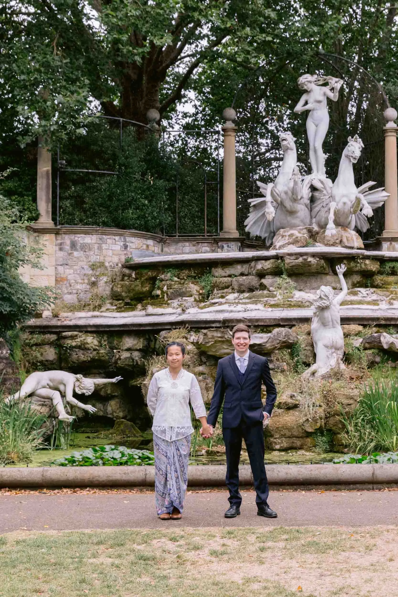 A couple stands in front of the "Naked ladies" fountain at York house gardens, following their wedding ceremony